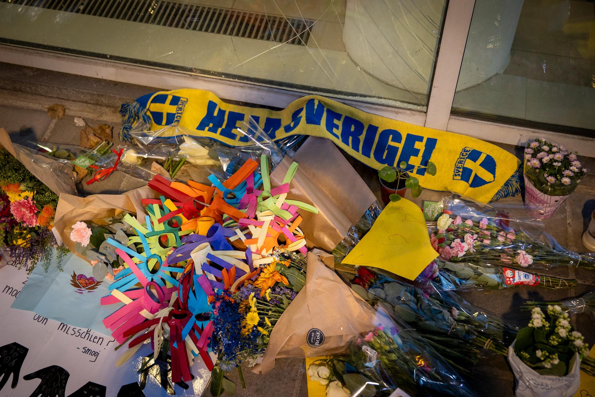 Minnesplats med blommor och en blågul halsduk med texten Heja Sverige på.