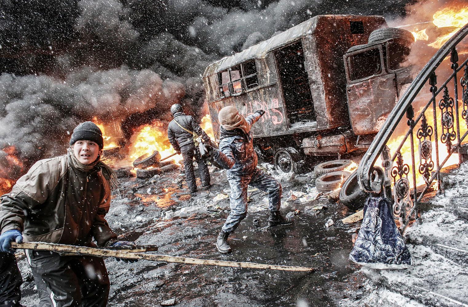 Demonstranter tar skydd bakom en utbränd lastbil medan de kastar bråte mot poliserna.