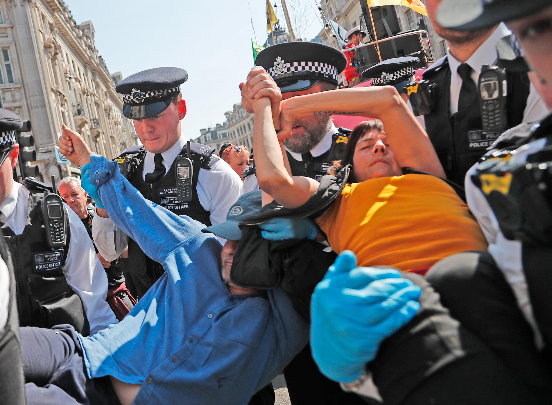 Poliser bär i väg ett par demonstranter som limmat ihop sina händer vid Oxford Circus i London på fredagen.
