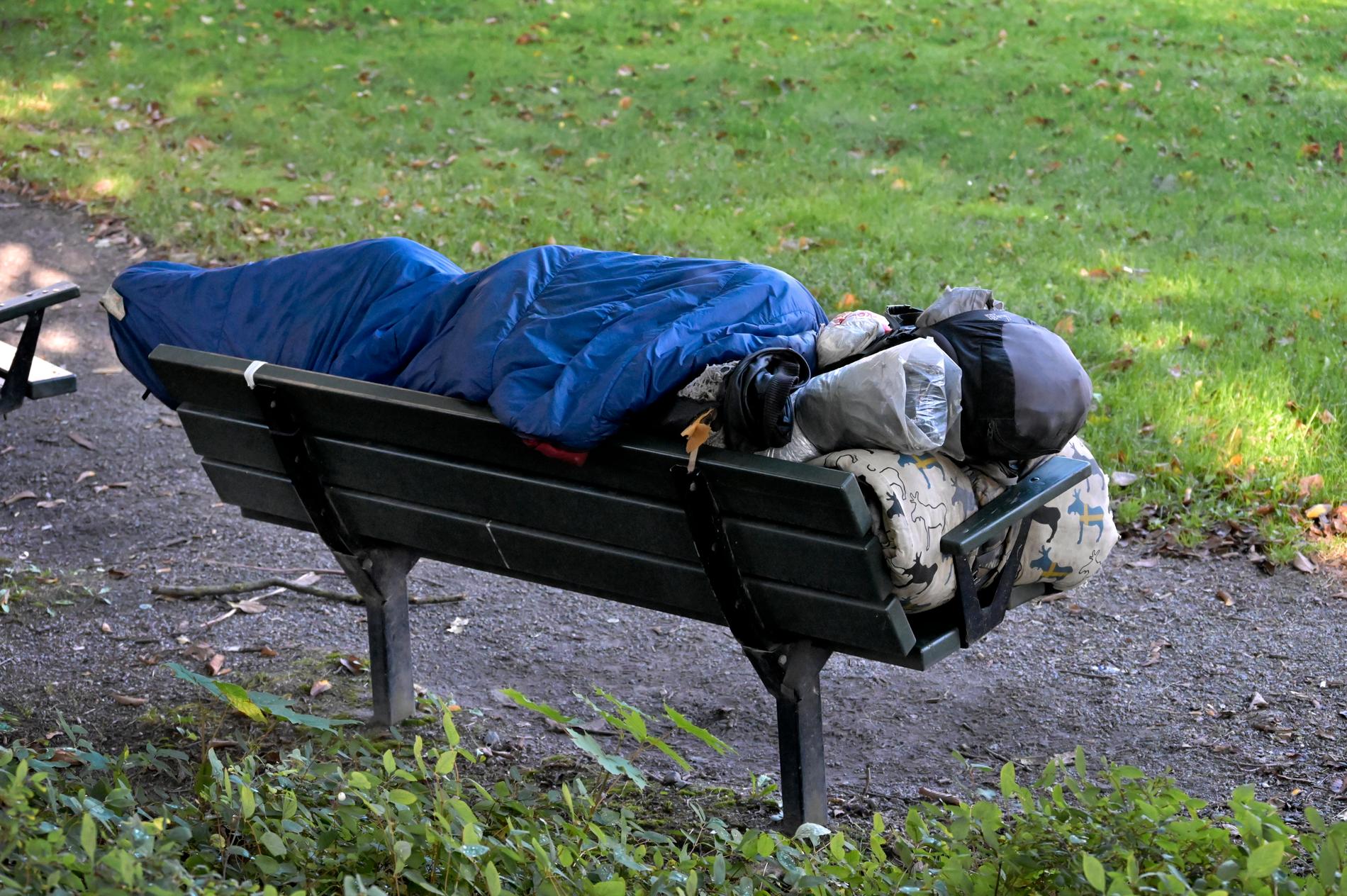En person ligger i en sovsäck på en bänk. 