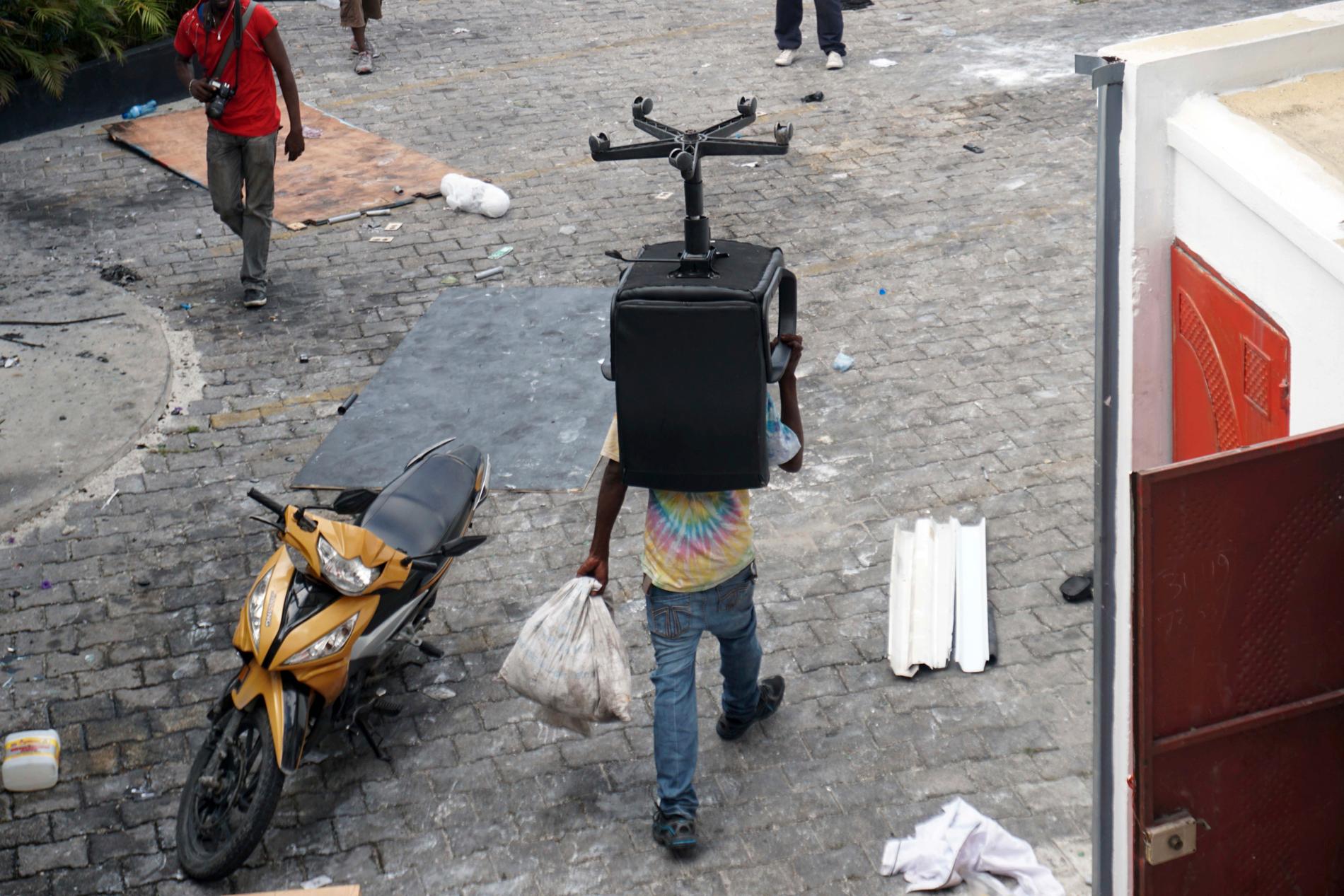En man i Port-au-Prince bär iväg på en stol under plundringarna av butiker i staden.