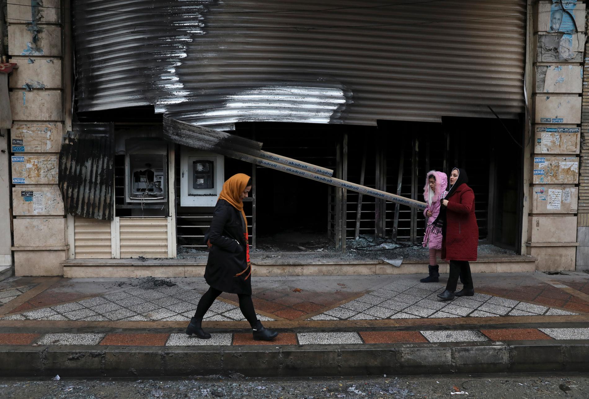 Lokalbor passerar förbi en bank i Shahriar i norra Iran som brandhärjats under protesterna. Arkivbild.