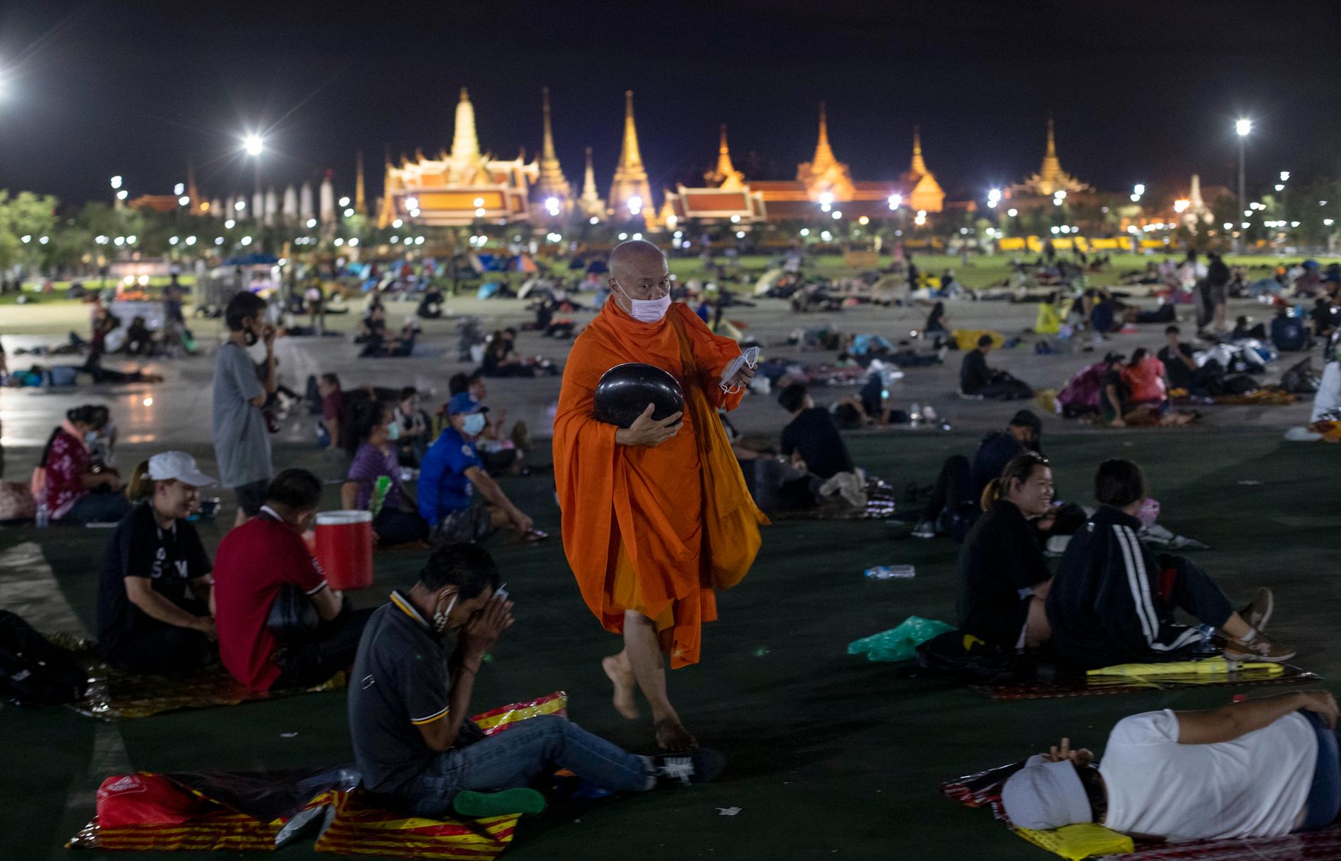 En buddhistmunk delar ut munskydd till de tusentals demonstranter som vägrade lämna Sanam Luang-torget, utanför det kungliga palatset i Bangkok, under natten till söndag.