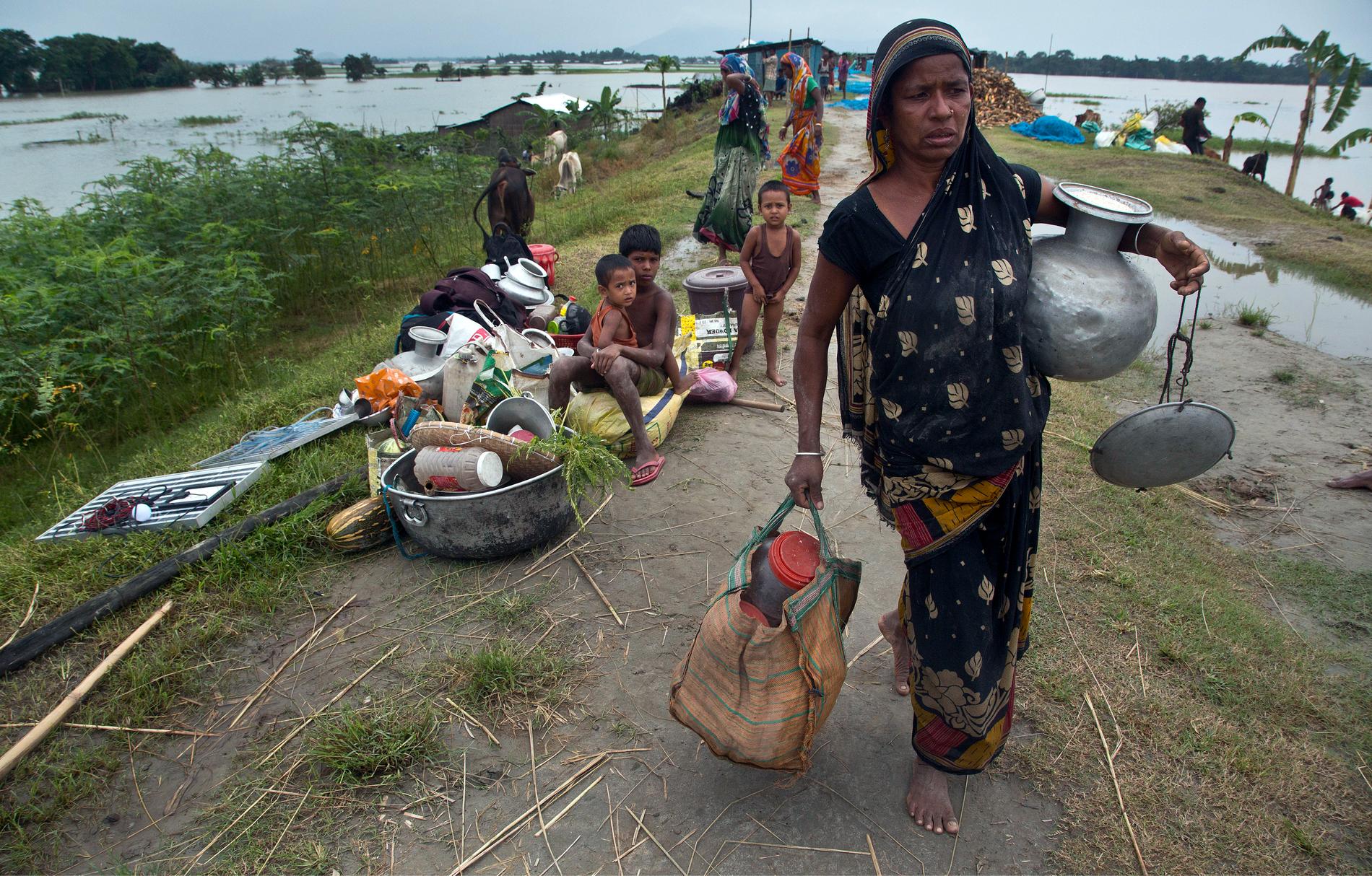 En indisk kvinna bär på sina saker när hon söker skydd från regnen i staden Guwahati i delstaten Assam.