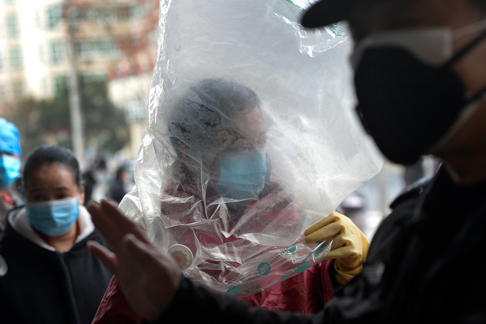 En man skyddar sig med ansiktsmask och en plastpåse över huvudet när han går in på en mataffär i Wuhan, Kina.