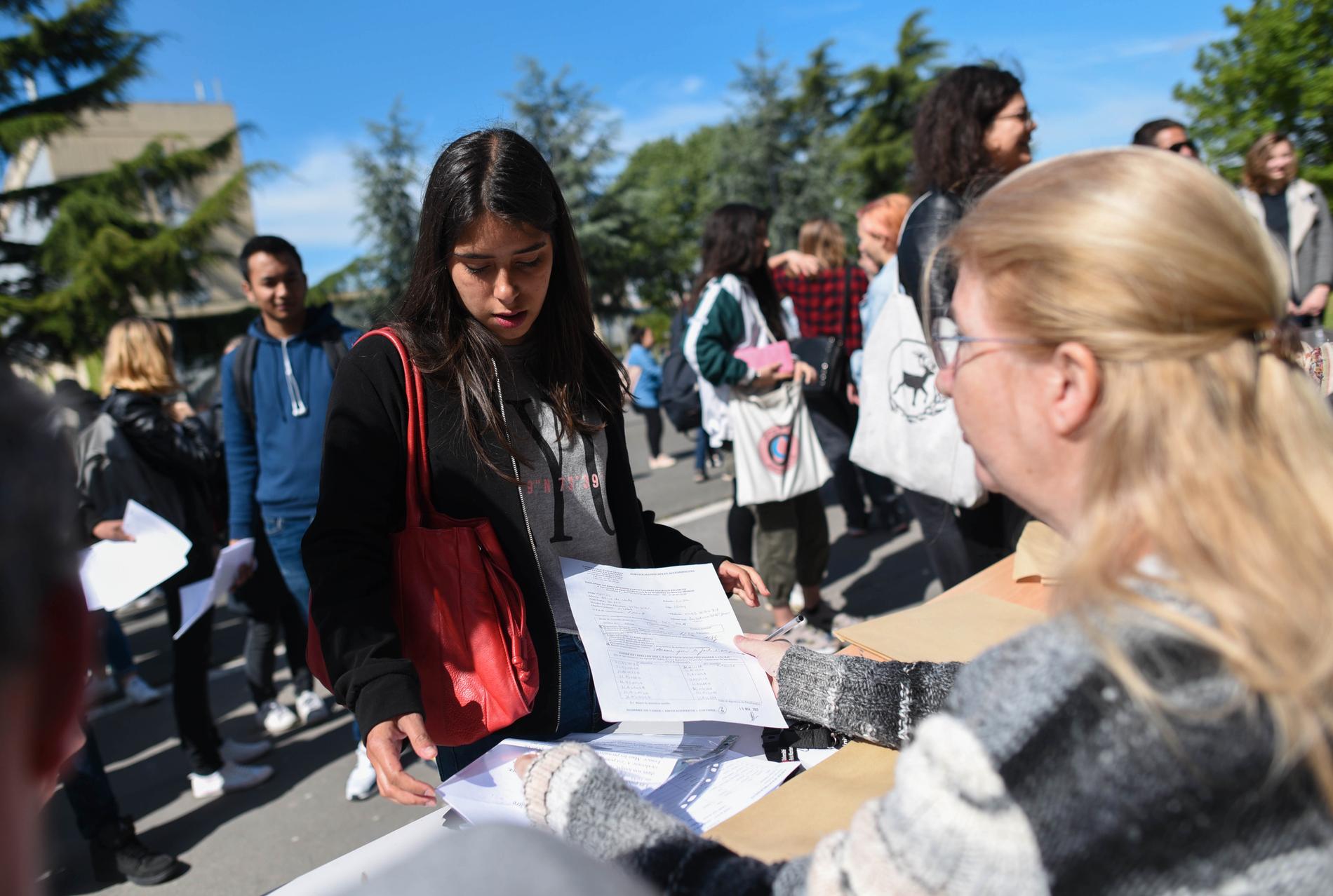Studenten Luisa Mejias lämnar in en hemtenta till sin lärare, som fått sätta upp bord utanför en ockuperad byggnad för att kunna ta emot elevernas uppgifter.