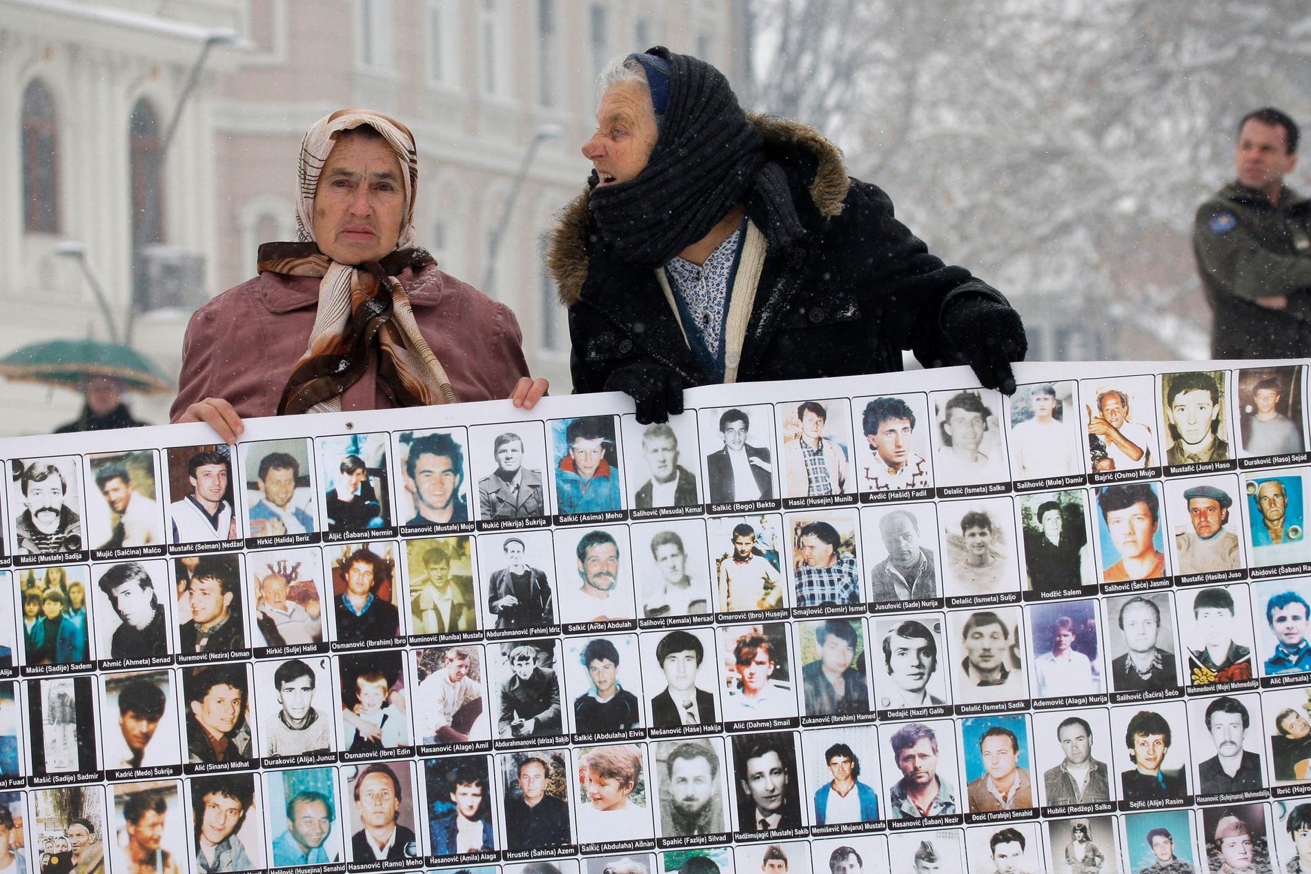 Två kvinnor håller upp bilder på offer från massakern i Srebrenica den 11 juli 1995