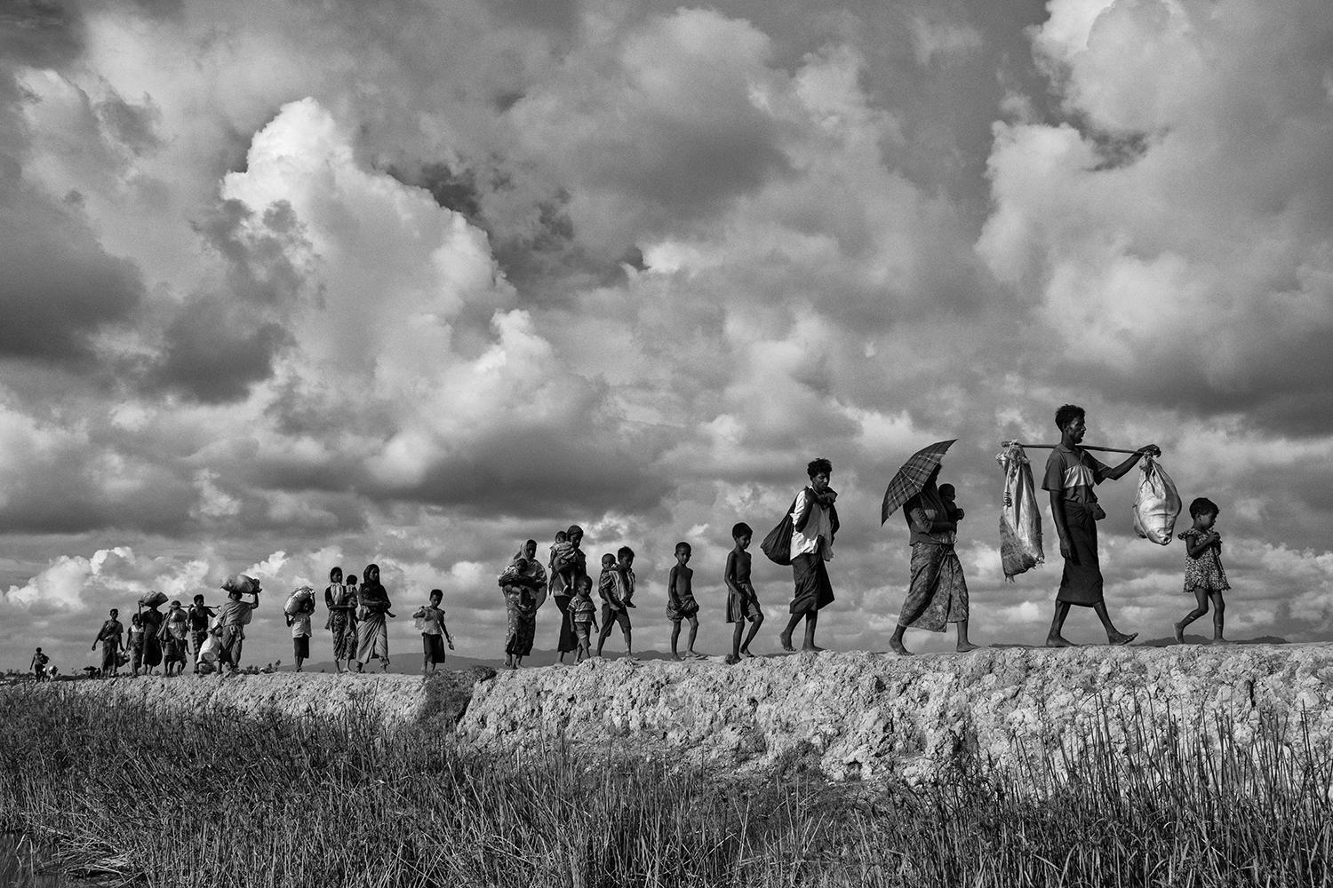Rohingyaflyktingar bär sina tillhörigheter när de går på Bangladesh-sidan av floden Naf efter att ha flytt Myanmar.