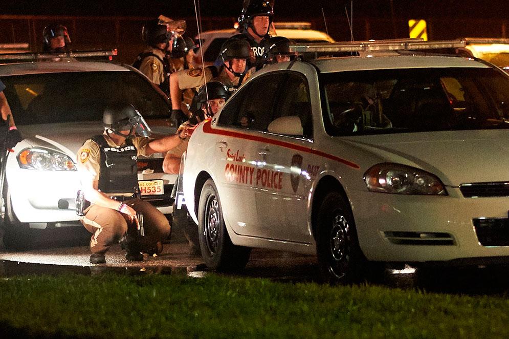 Poliser tar skydd bakom en bil i Ferguson.