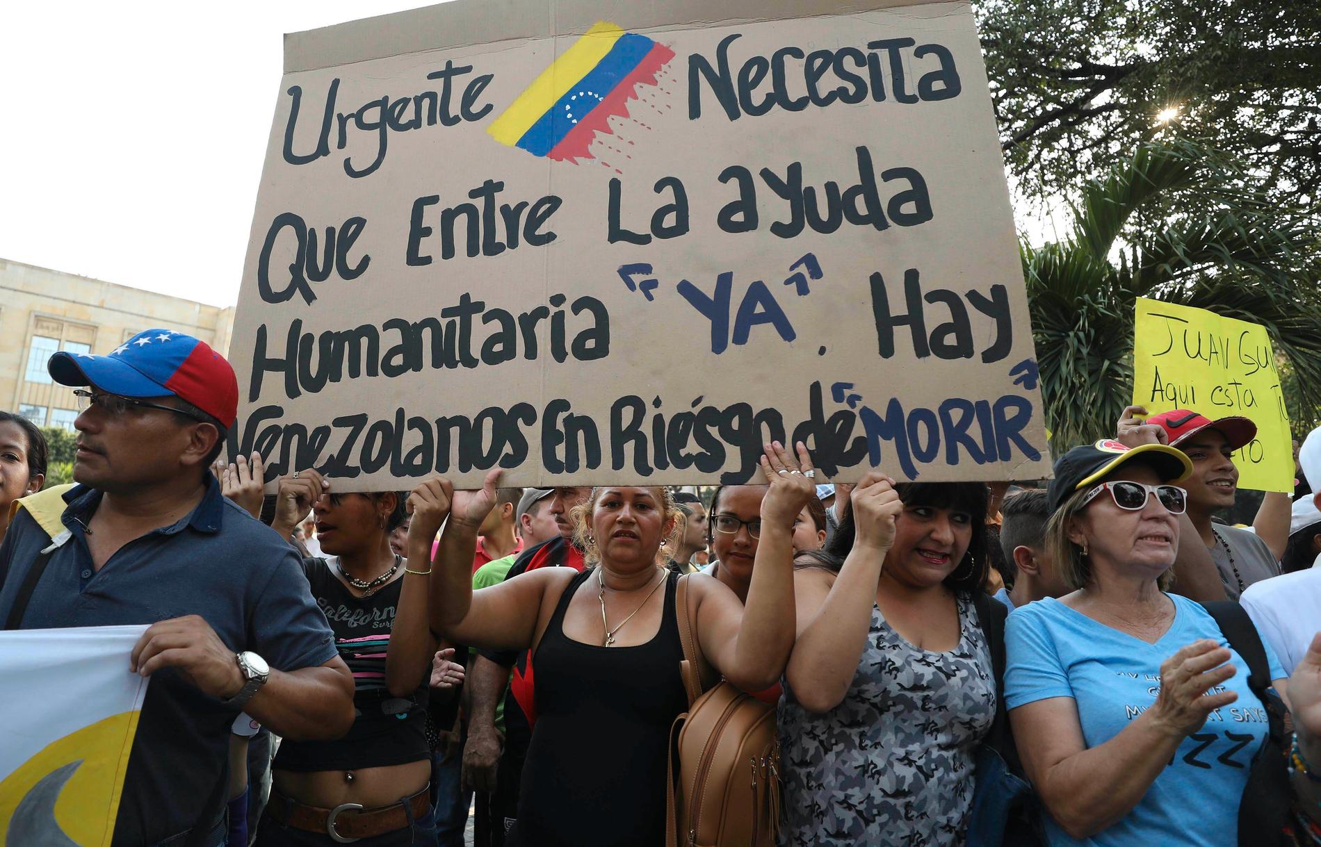 Venezuelaner i den colombianska staden Cúcuta kräver att man ska släppa in humanitär hjälp i Venezuela. På skylten står det: "Brådskande. Humanitär hjälp måste släppas in nu. Venezuelaner riskerar att dö".