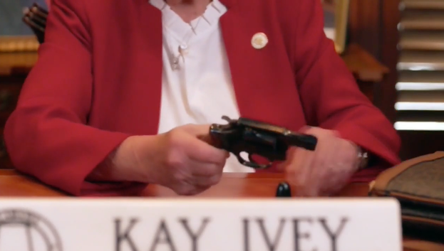 Guvernören Kay Ivey (R) plockar fram en revolver ur sin väska.