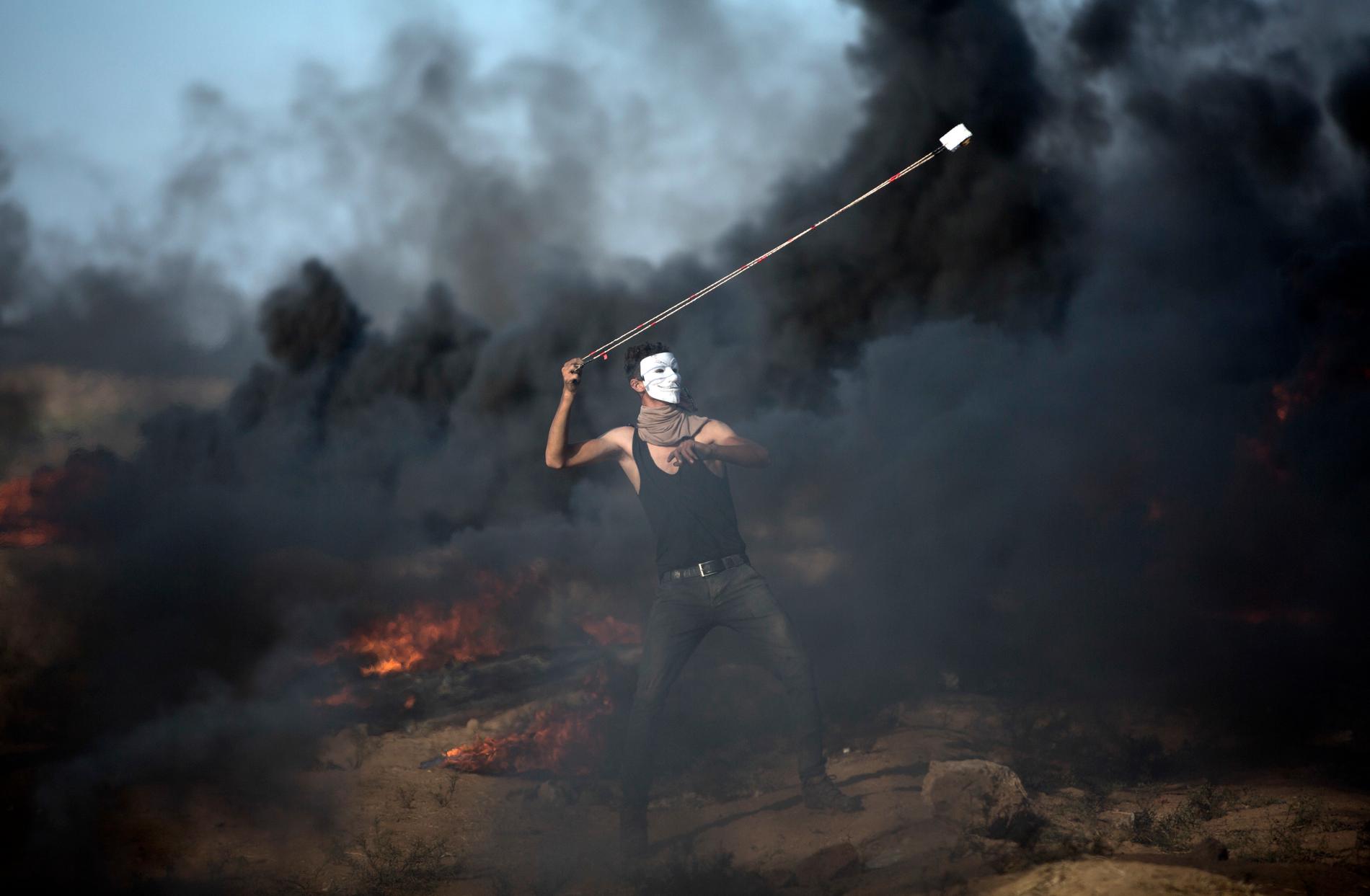 En palestinsk man slungar stenar mot israeliska trupper vid Gazagränsen.