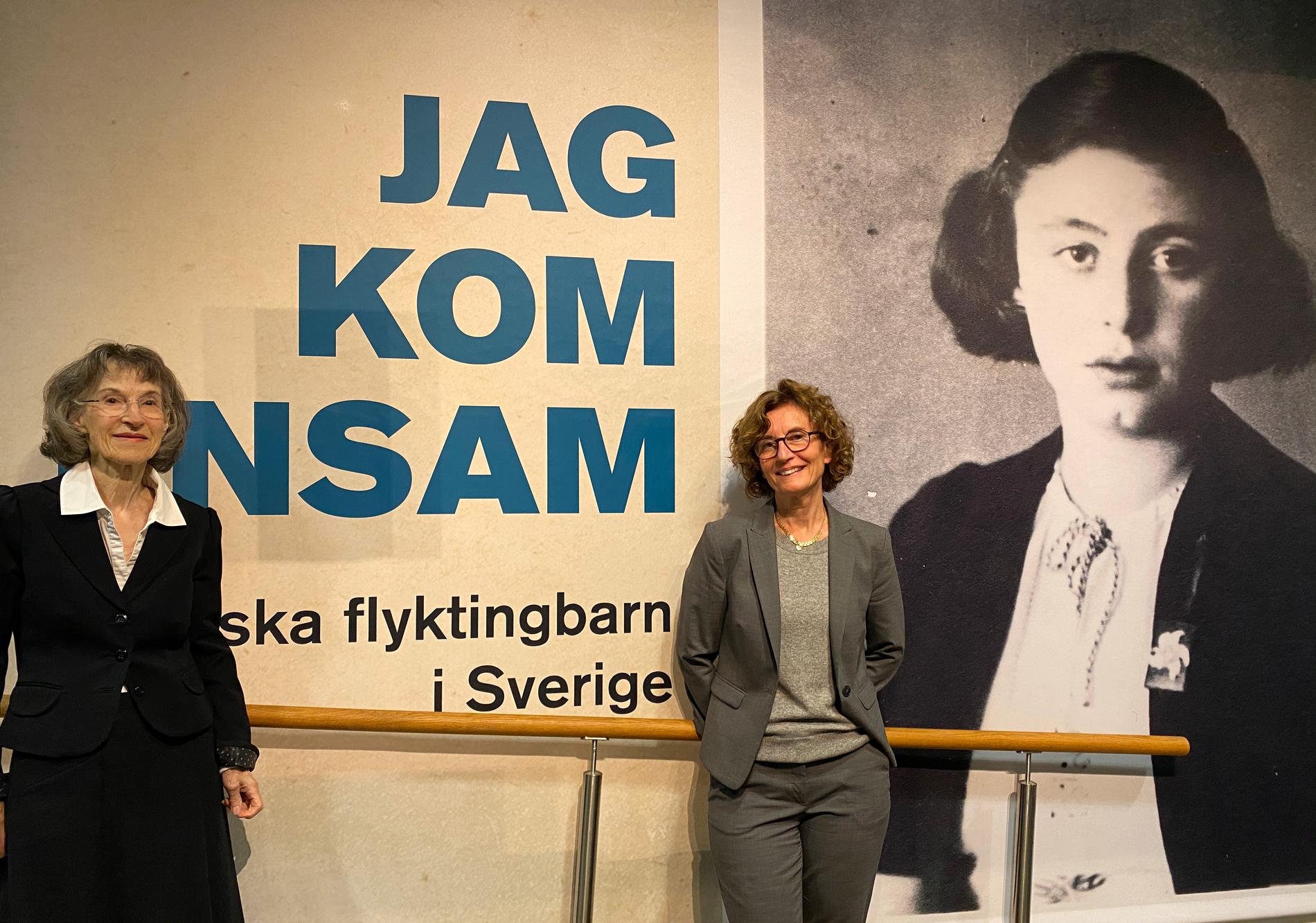 Eva Lecerof och Ingrid Lomfors vid utställningen ”Jag kom ensam”. Ingrid Lomfors mamma Penina, som kom ensam till Sverige som 13-åring, syns på den svartvita bilden till höger.