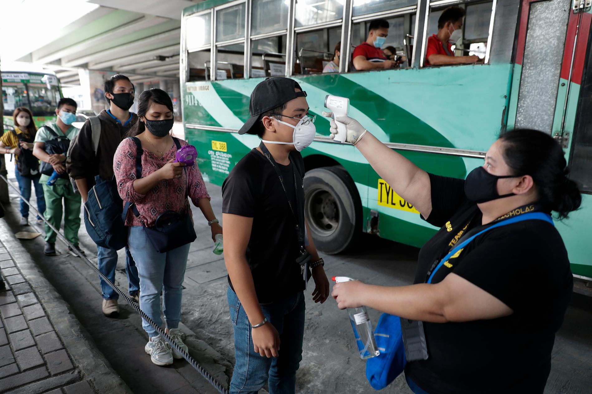 Passagerare får sin kroppstemperatur kontrollerad innan de går ombord en buss under den första dagen av lättade restriktioner i Manila på måndagen.