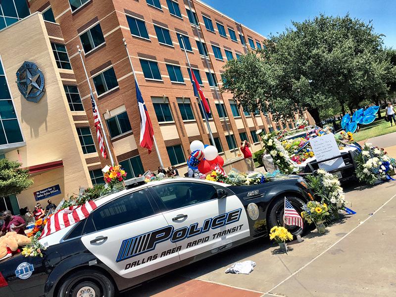 Två polisbilar parkerade framför entrén har överösts med blommor, kramdjur och kärleksfulla meddelanden.