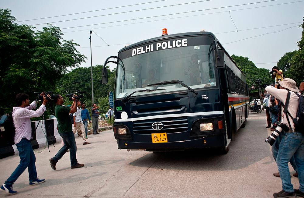 Journalister fotograferar polisbussen med de åtalade.