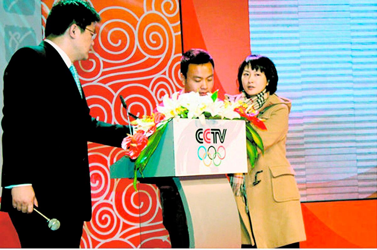 HÄMND I RUTAN Kinesiska stats-tv:n inviger sin OS-kanal. Zhang Bin (till vänster)får äran att vara programledare för premiärsändningen. Plötsligt rusar hans fru, som också är känd programledare i kinesisk tv, fram till talarstolen och avslöjar att hennes man varit otrogen. Hon hinner säga mycket innan hon motas ut.