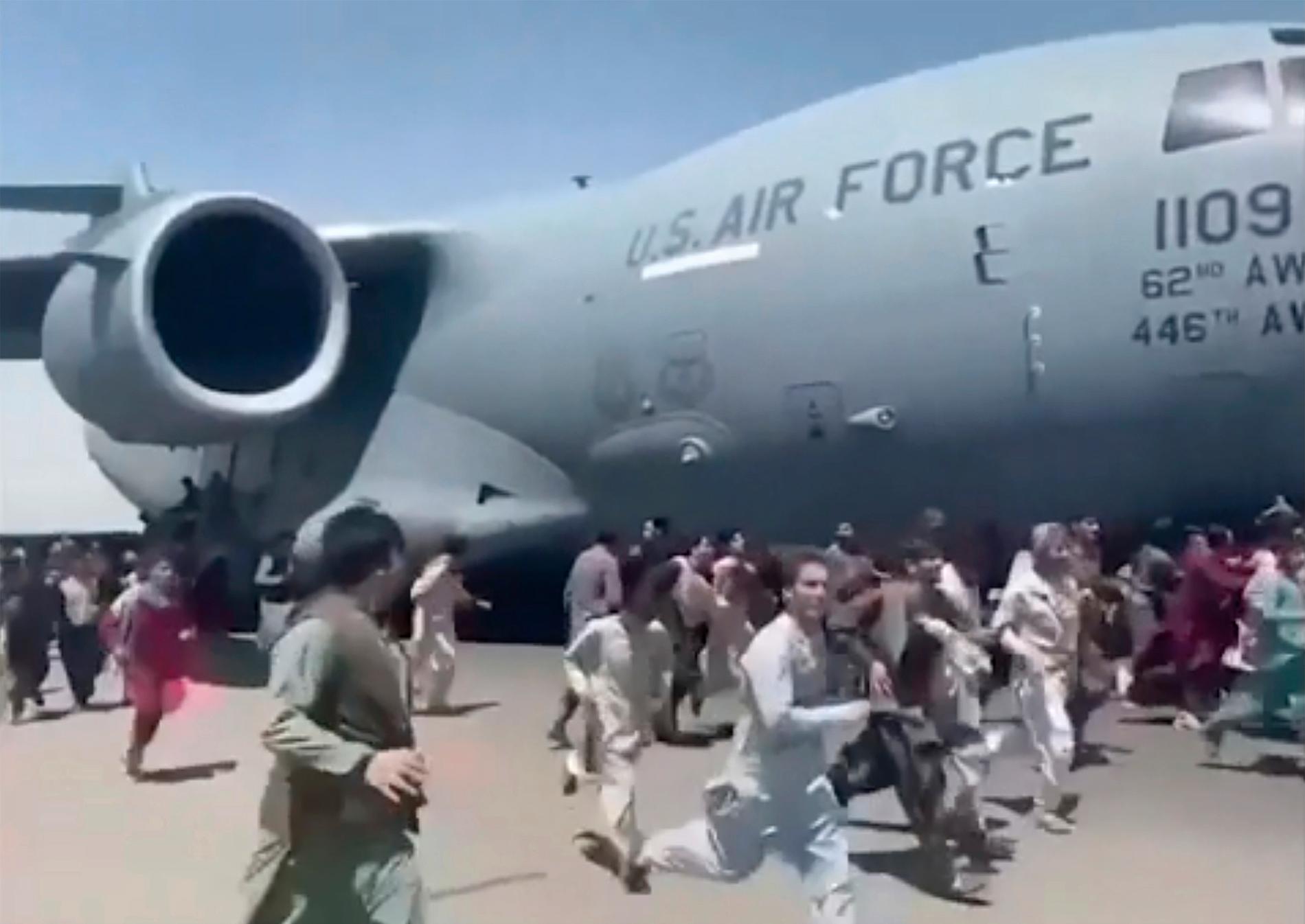 Människor springer bredvid och klamrar sig fast vid ett amerikanskt militärflygplan som sedan lyfter får flygplatsen i Kabul.