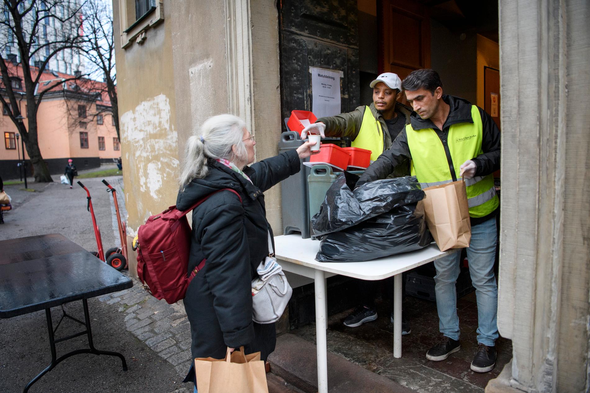 Mia Johansson får en kopp kaffe och en påse med mat av Bajo Gabrimariam och Wahid Nafipour vid St:a Clara kyrka, som delar ut mat till hemlösa.