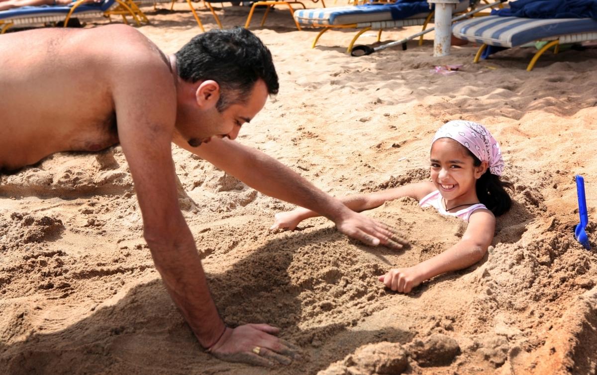Priya Deva, 8, blir nergrävd i sanden av pappa Jay Deva på stranden i Sharm El Sheikh.