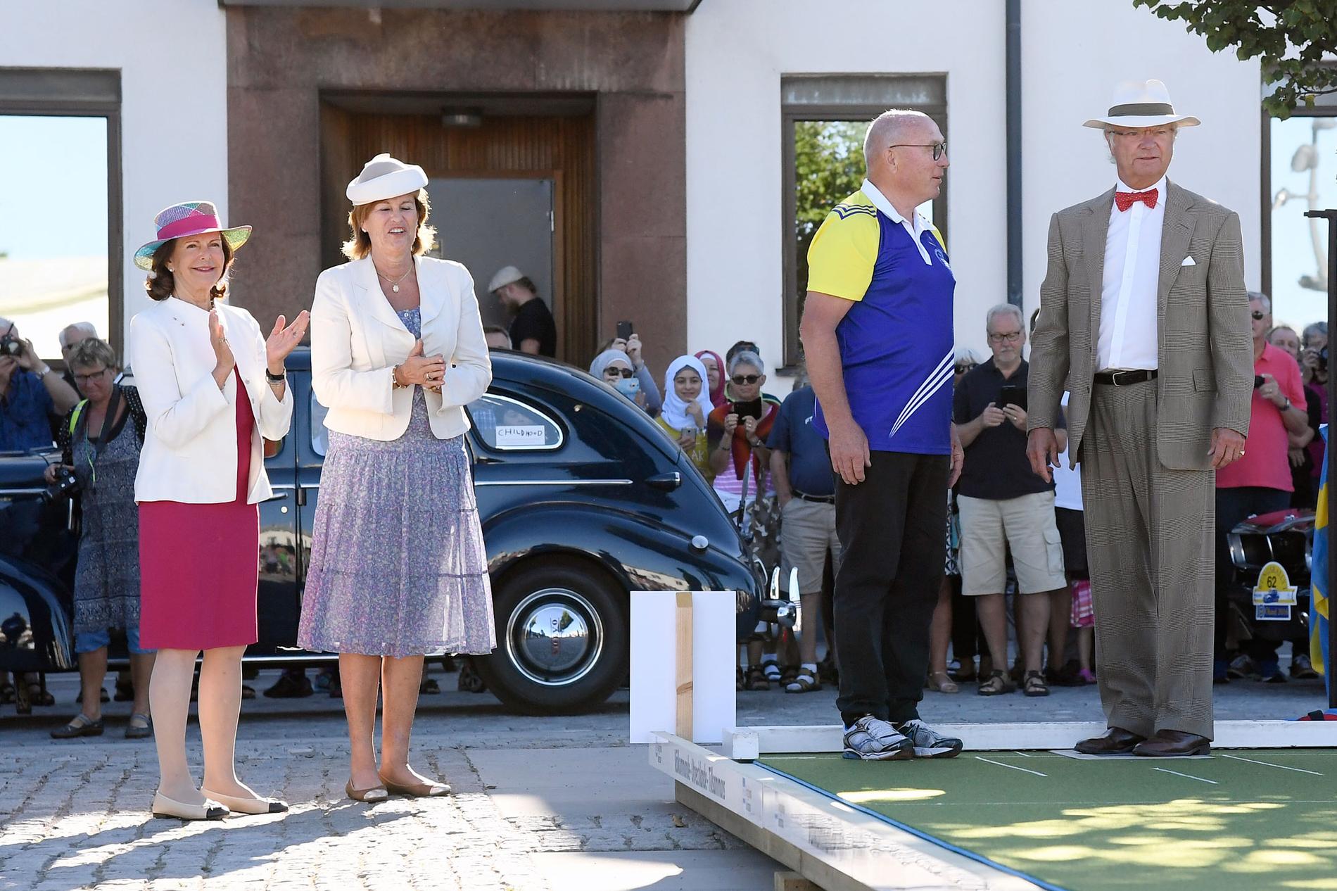 Drottning Silvia hejar på medan kungen spelar lawn bowls, en brittisk variant av boule, vid första kontrollen under rallyt.