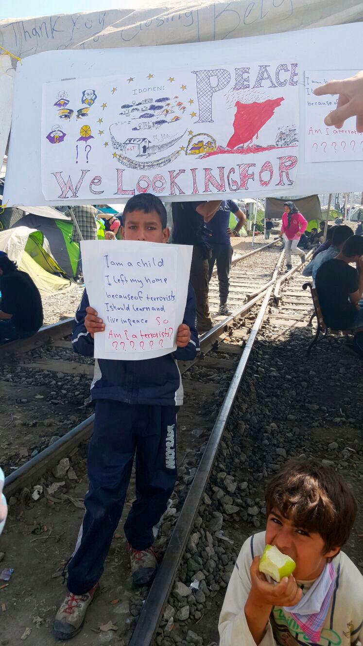 En pojke håller upp en lapp med texten att han flytt från terrorister men att han nu pekas ut som terrorist själv.