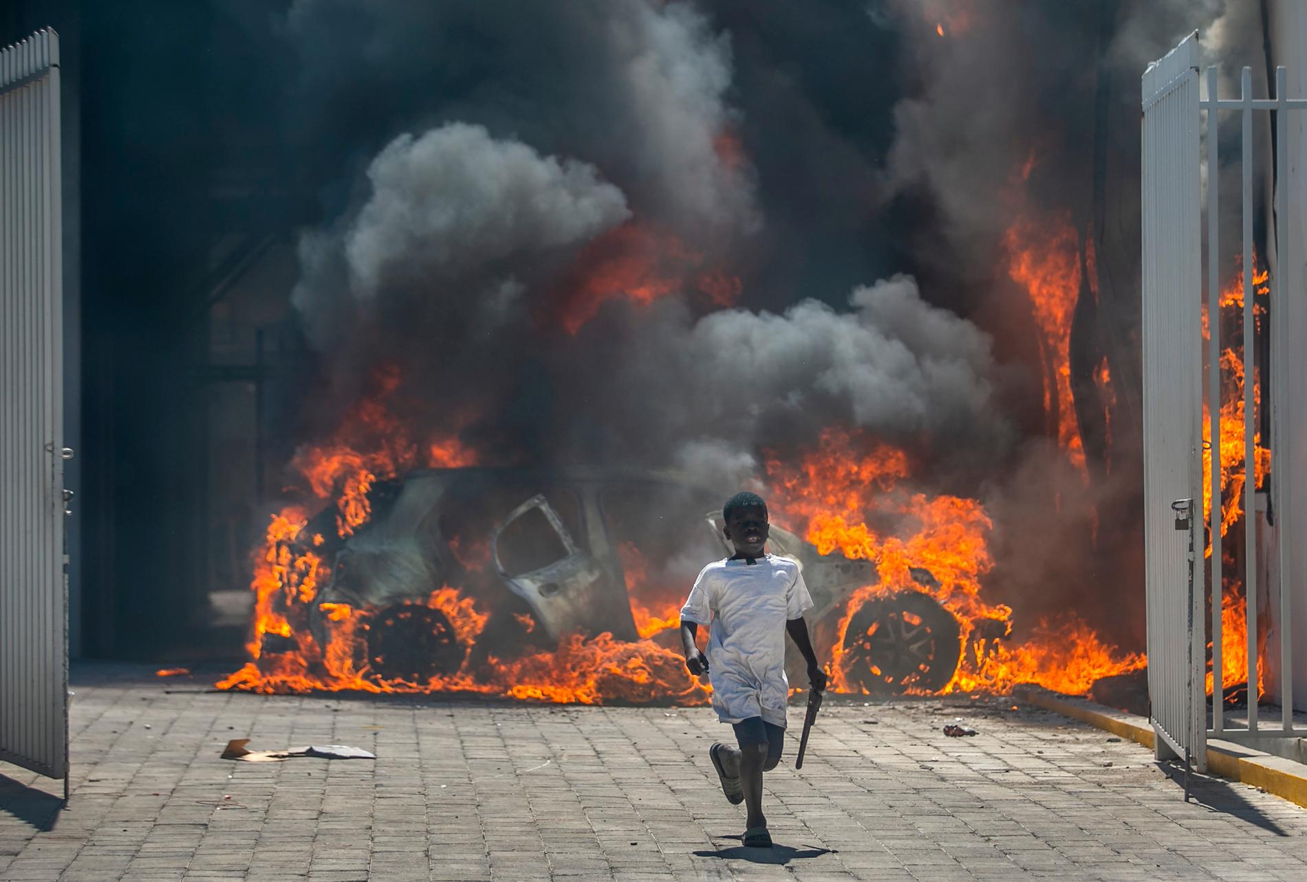 En pojke flyr från en bilhandel som satts i brand under demonstrationer i Port-au-Prince i mars i år.