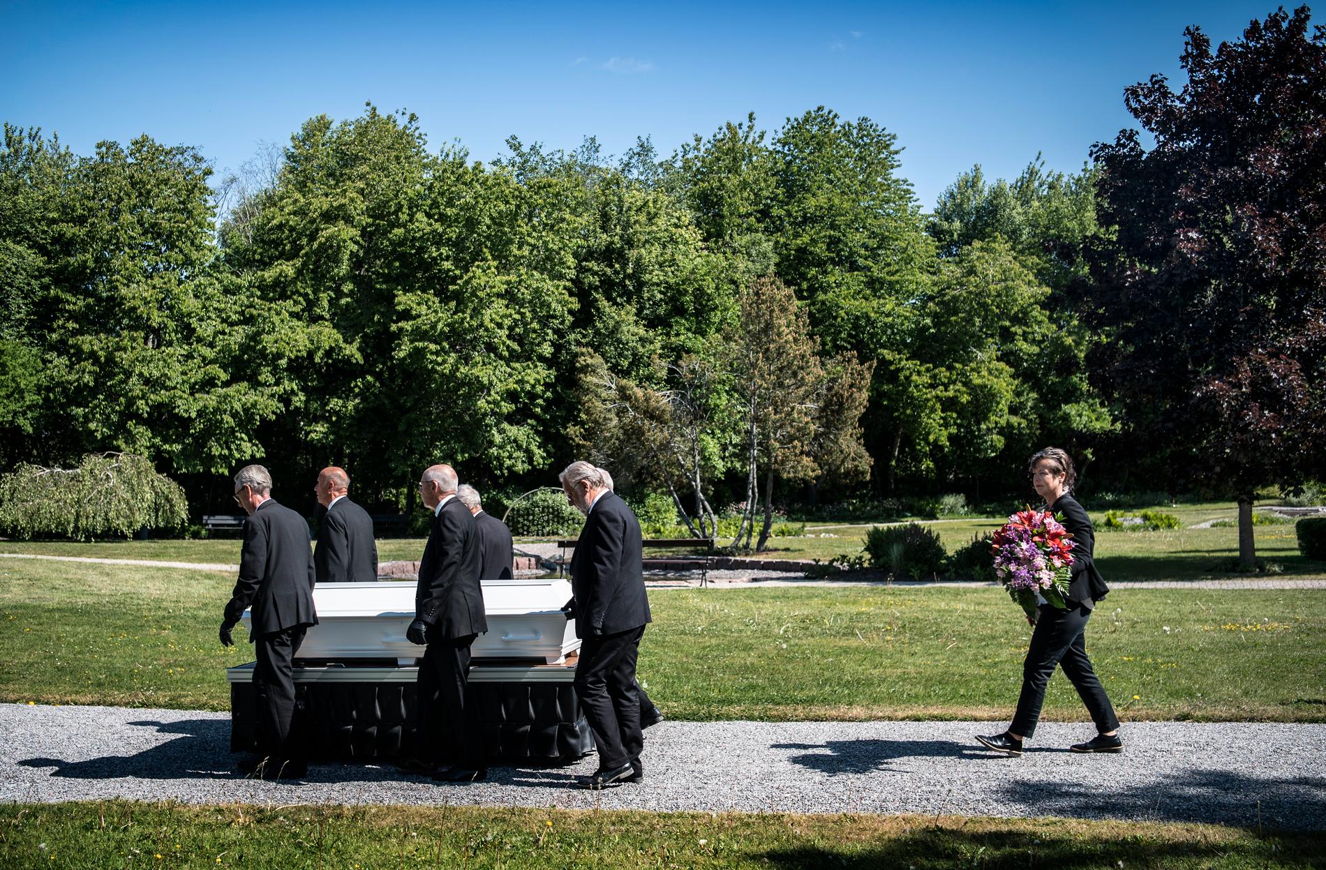 Sex män i svarta kostymer bär kvinnans kista mot graven.