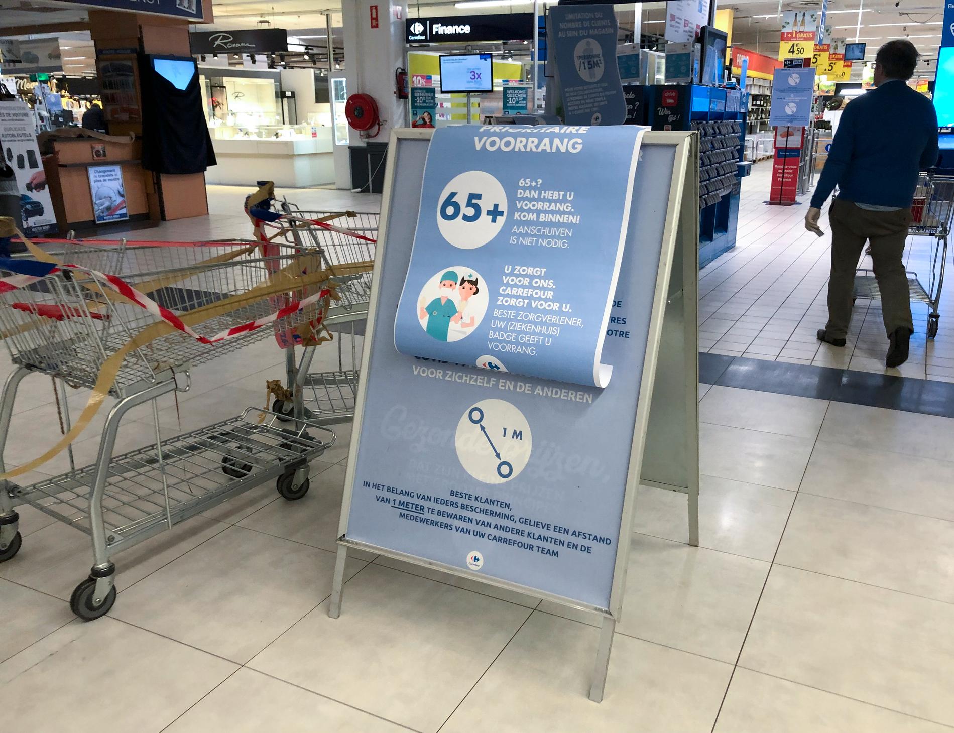 Skyltar i en belgisk matvarubutik manar till minst en meters avstånd mellan kunderna – och ger pensionärer och vårdanställda rätt att gå före i kön.