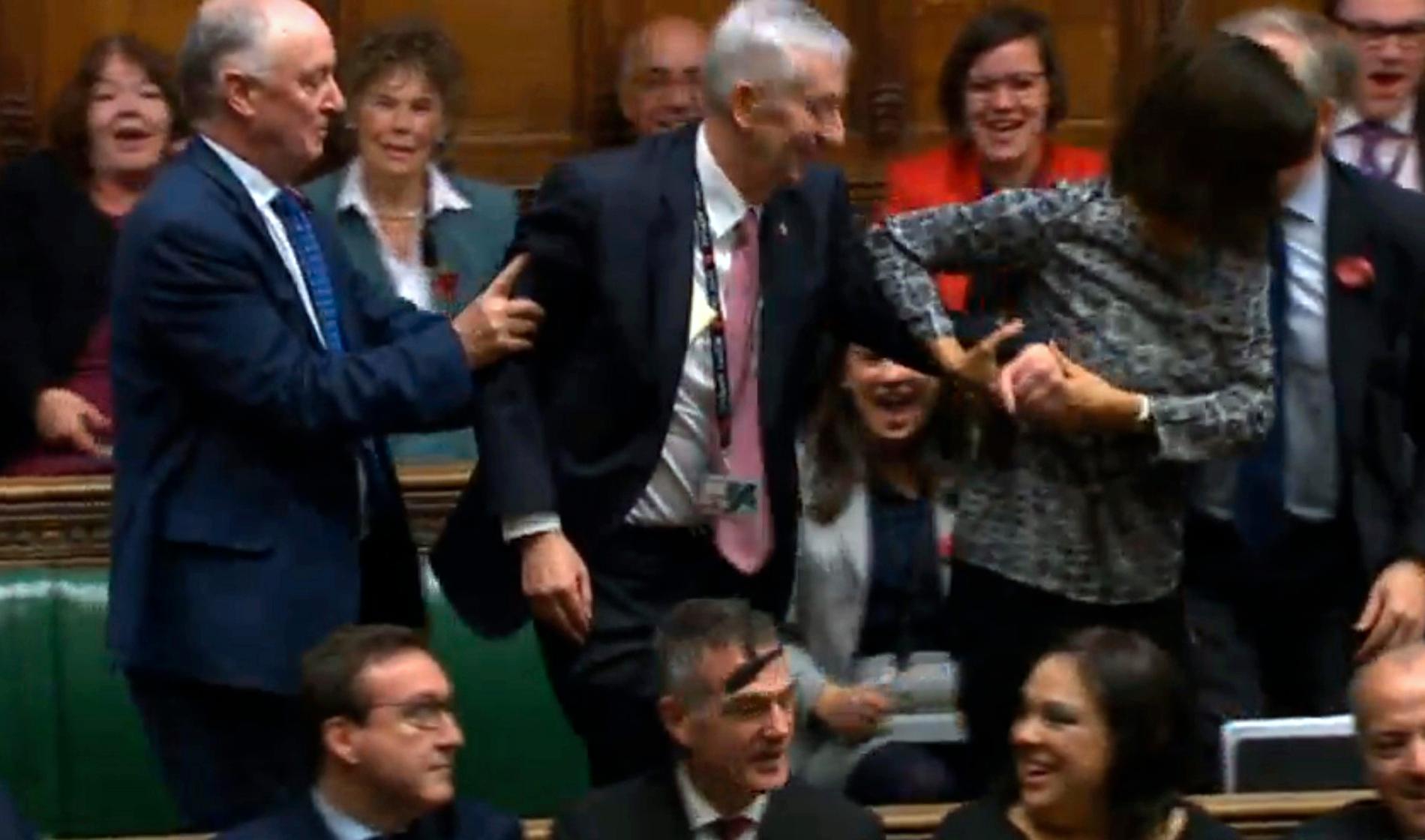 Storbritanniens nyvalde talmann Lindsay Hoyle, i mitten, släpas – enligt en gammal tradition– till talmansstolen av två av sina anhängare.