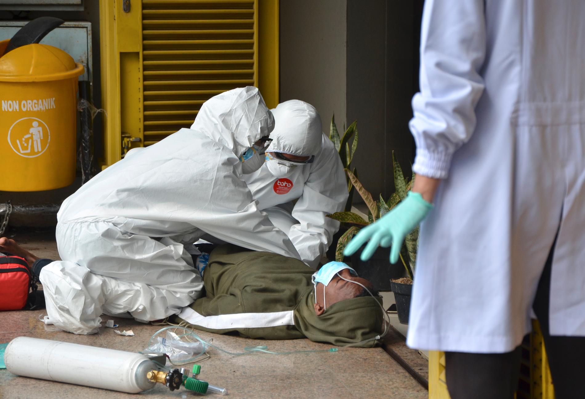 Vårdpersonal i skyddsutrustning mot coronavirus tittar till en man som kollapsat vid en vårdinrättning i Indonesiens huvudstad Jakarta.