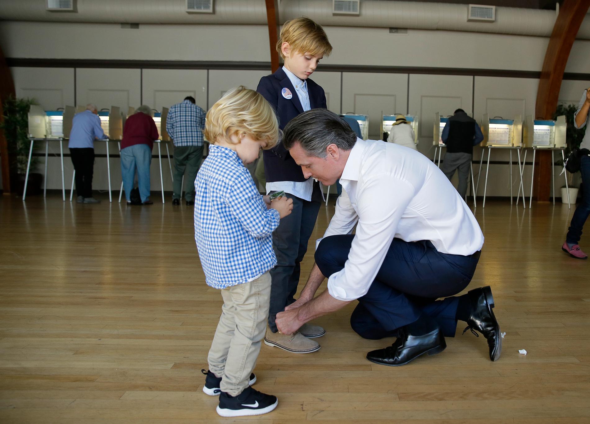 Guvernörskandidaten Gavin Newsom (D) hjälper sin son Hunter, 7, med skorna i röstlokalen i Larkspur, Kalifornien.