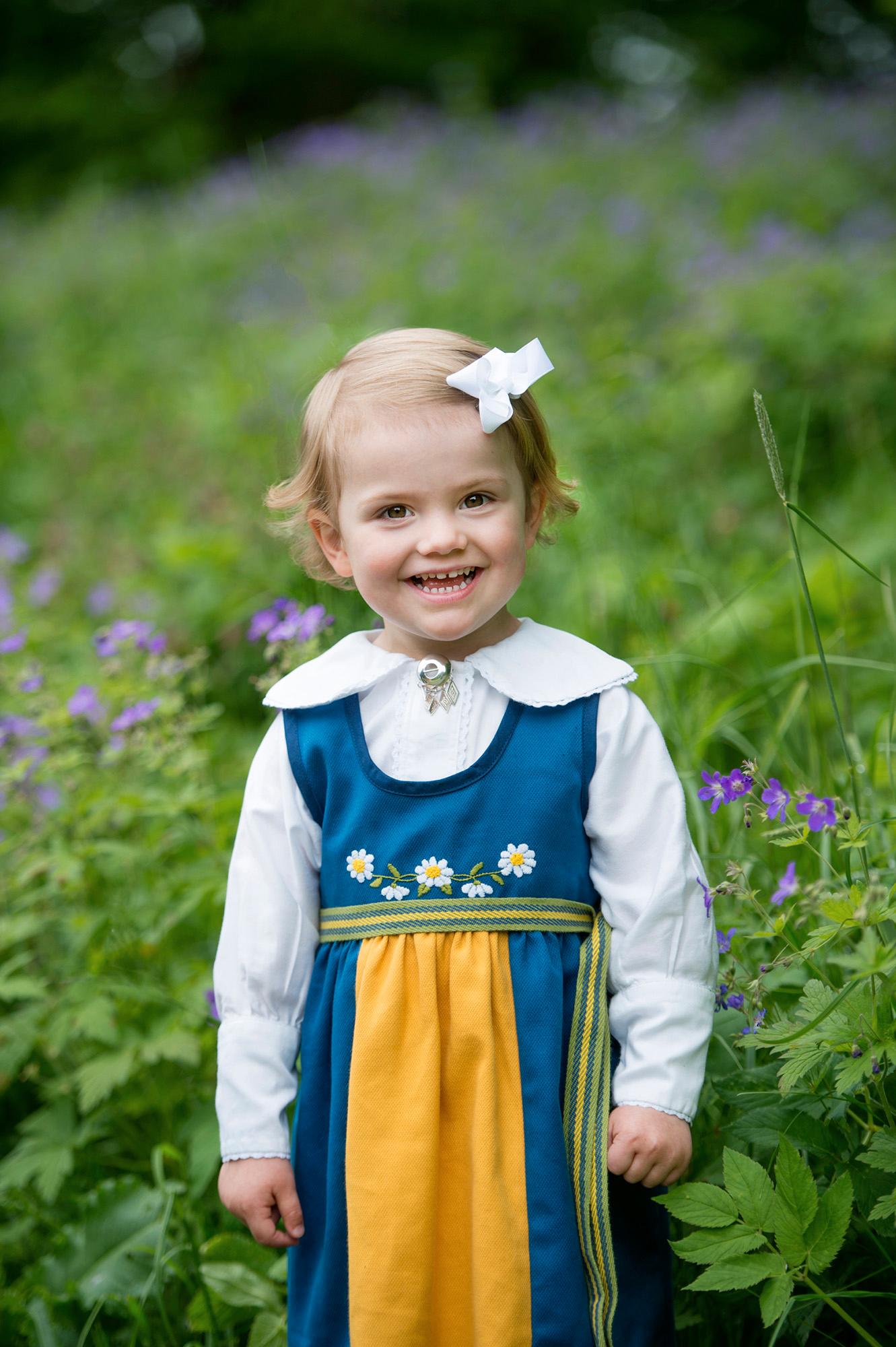 En glad liten tjej på nationaldagen iklädd Sverigedräkt i miniatyrformat.