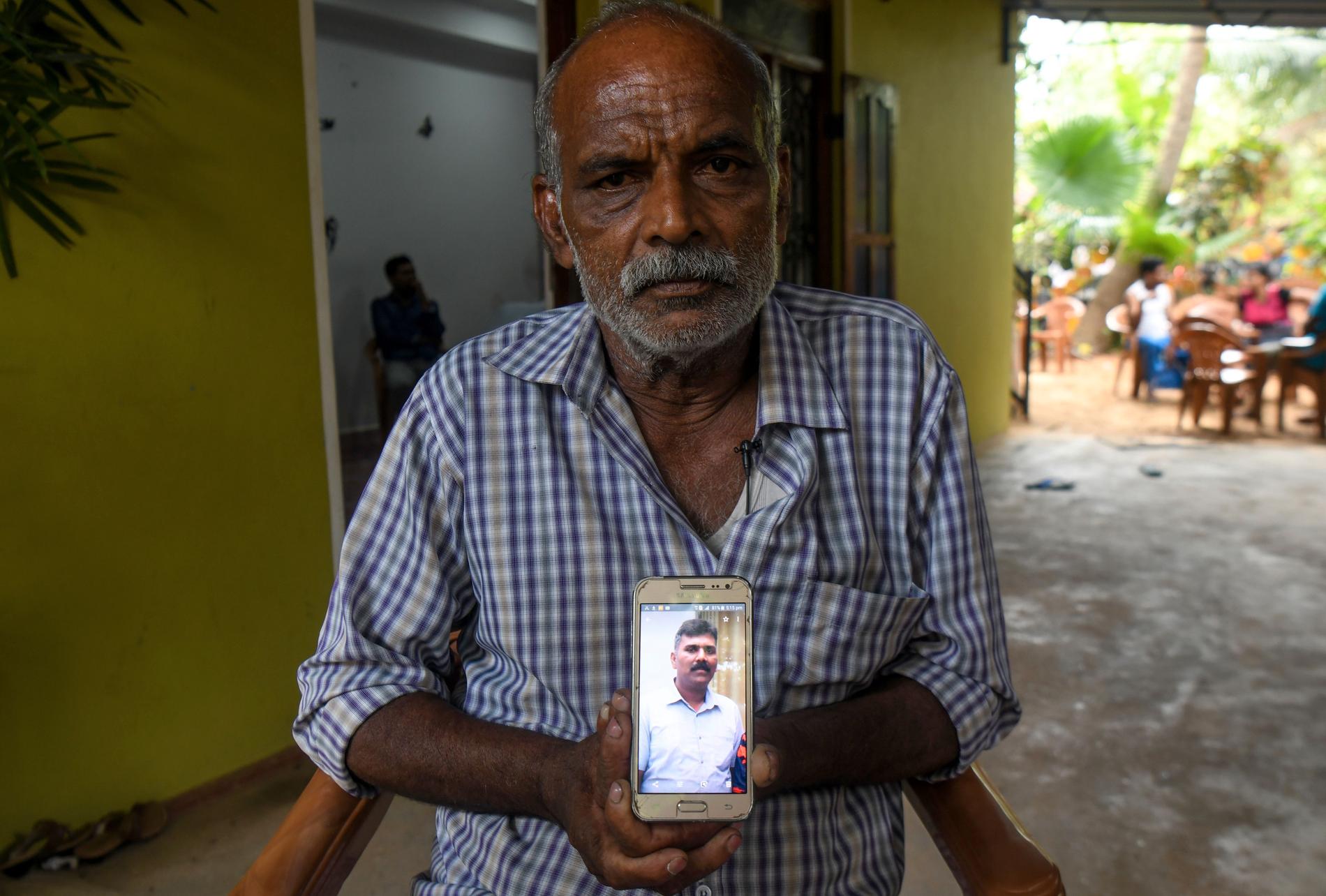 Velusami Raju håller upp en bild på sin telefon av sin son Ramesh Raju som dog i ett av attentaten.