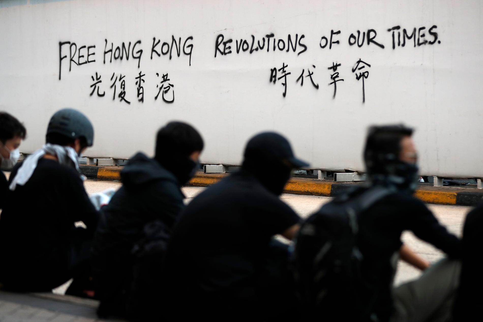Demonstranter vid en vägg som sprejats med slagord.