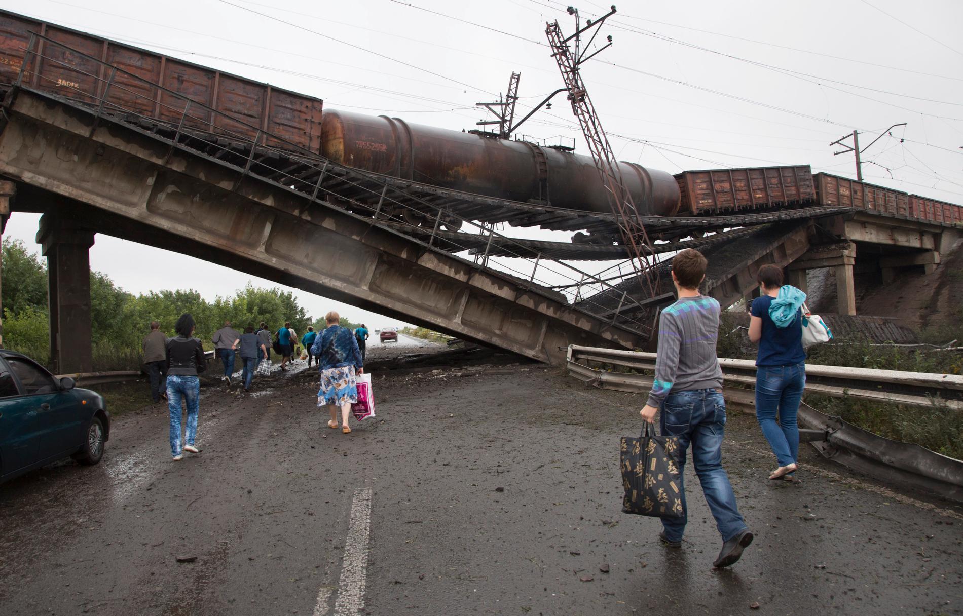 Människor går under en förstörd järnvägsbro nära byn Novobakhmutivka 20 kilometer norr om Donetsk, måndag 7 juli 2014. 
Bron har förstörts för att blockera en viktig rutt till den rebellstyrda staden.