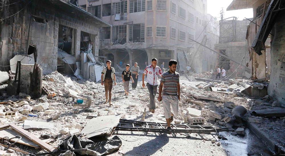 Personer undersöker en plats i staden Aleppo skadad av vad aktivister hävdar var en tunnbomb släppt av styrkor trogna Bashar al-Assad.