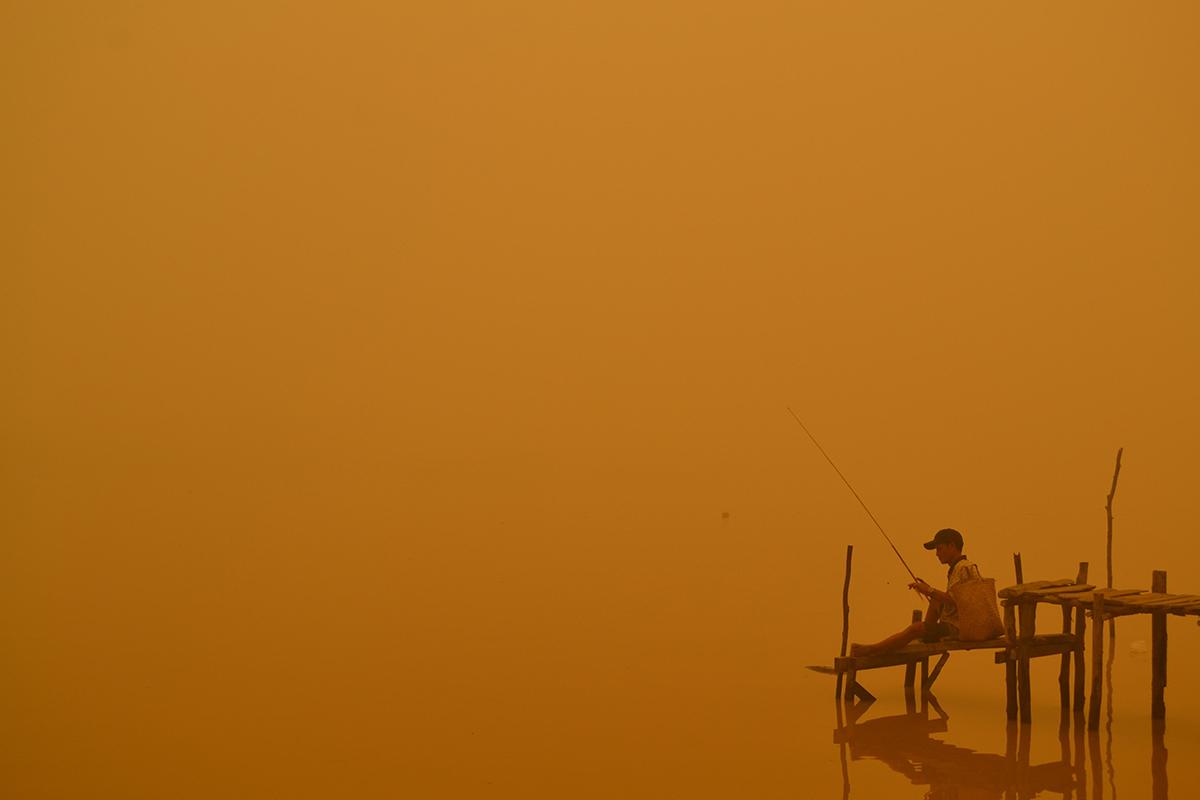 Palangkaraya City, Indonesien: En fiskande man sitter i röken efter flera skogsbränder i ö-riket. Skogsbränderna i området beräknas avge mer växthusgaser varje dag än hela USA:s industriella produktion.