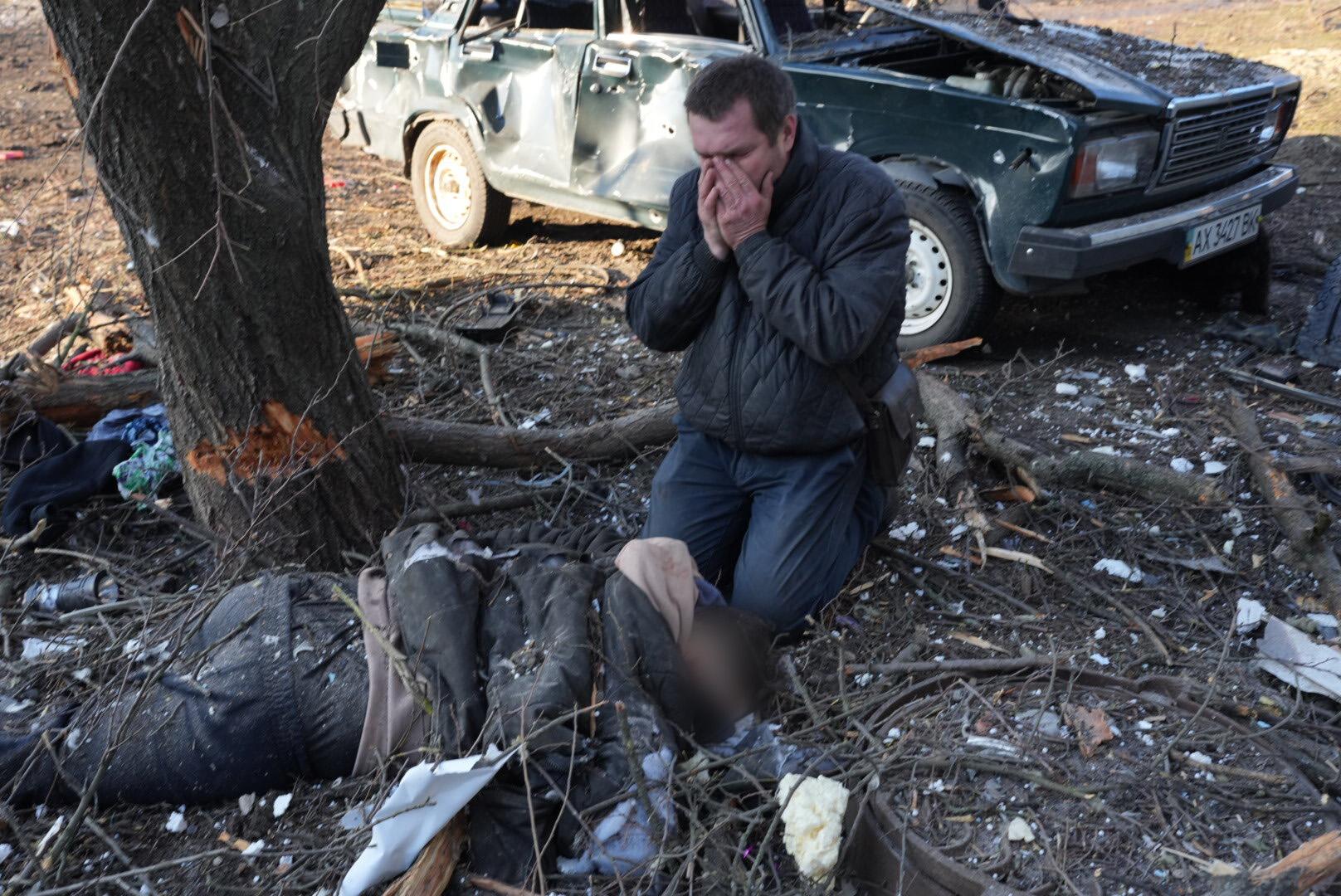 En man sitter sörjandes intill en kropp efter att ett lägenhetshus utanför Charkiv utsatts för flyganfall, den 24 februari. 