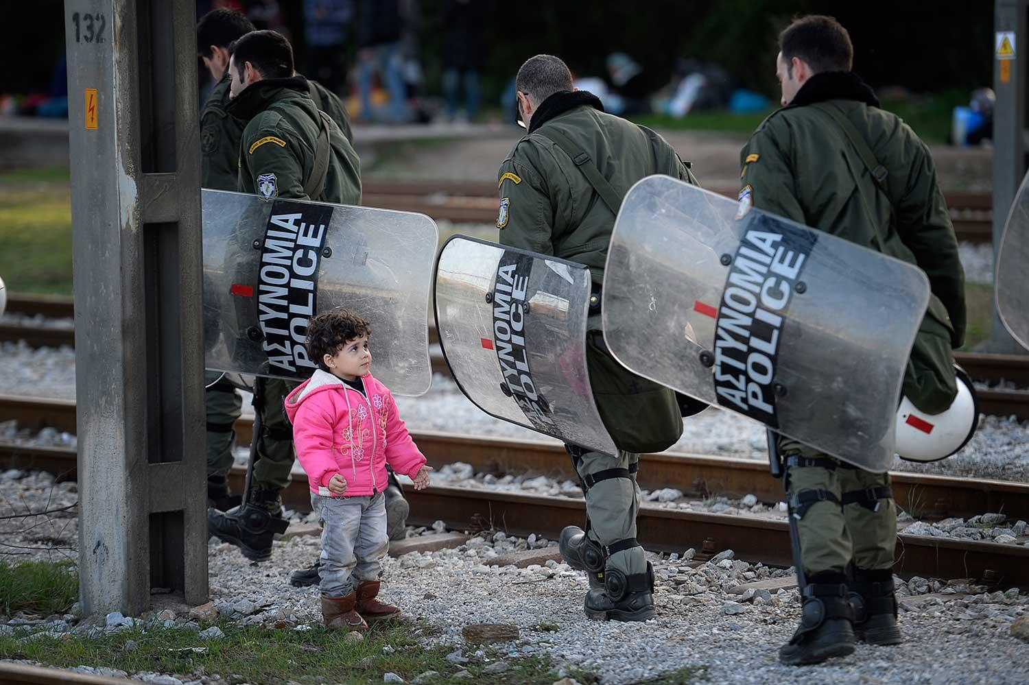 Kravallutrustade grekiska poliser passerar Rayenne Haj Khalaf, 3, som leker vid spåret.