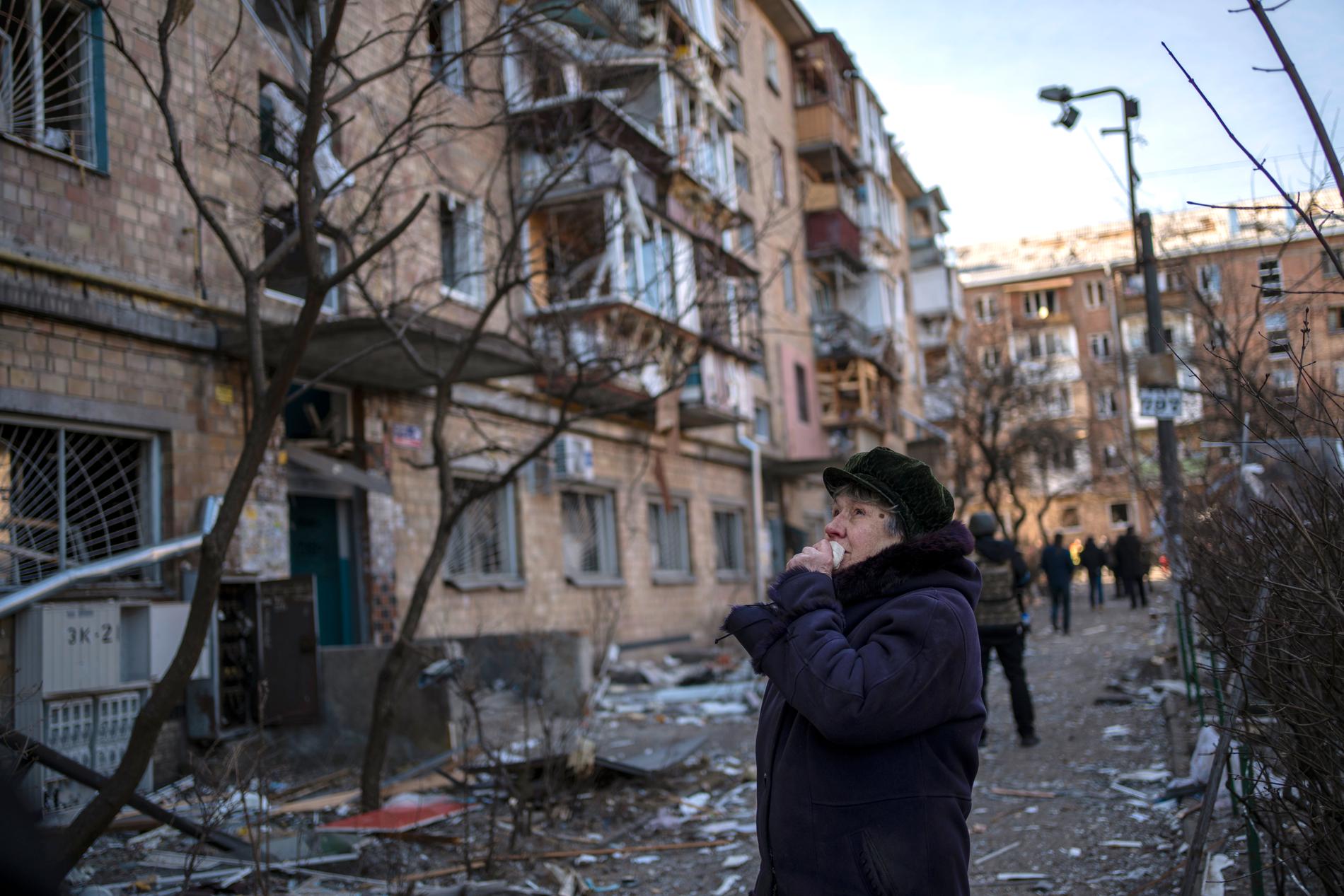 En kvinna gråter framför ett sönderbombat bostadshus i Kiev.