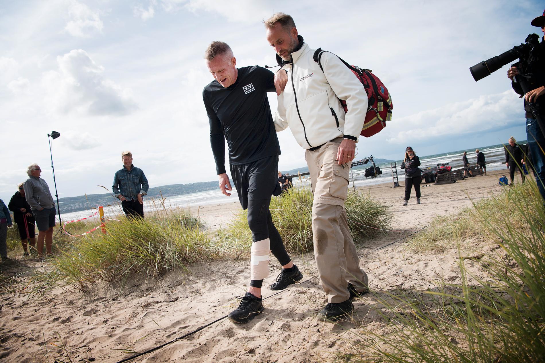 Bengt Gustafsson haltar från stranden med hjälp av SVT:s sjukvårdare.