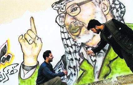 Två män lägger sista handen vid ett Arafat-porträtt.