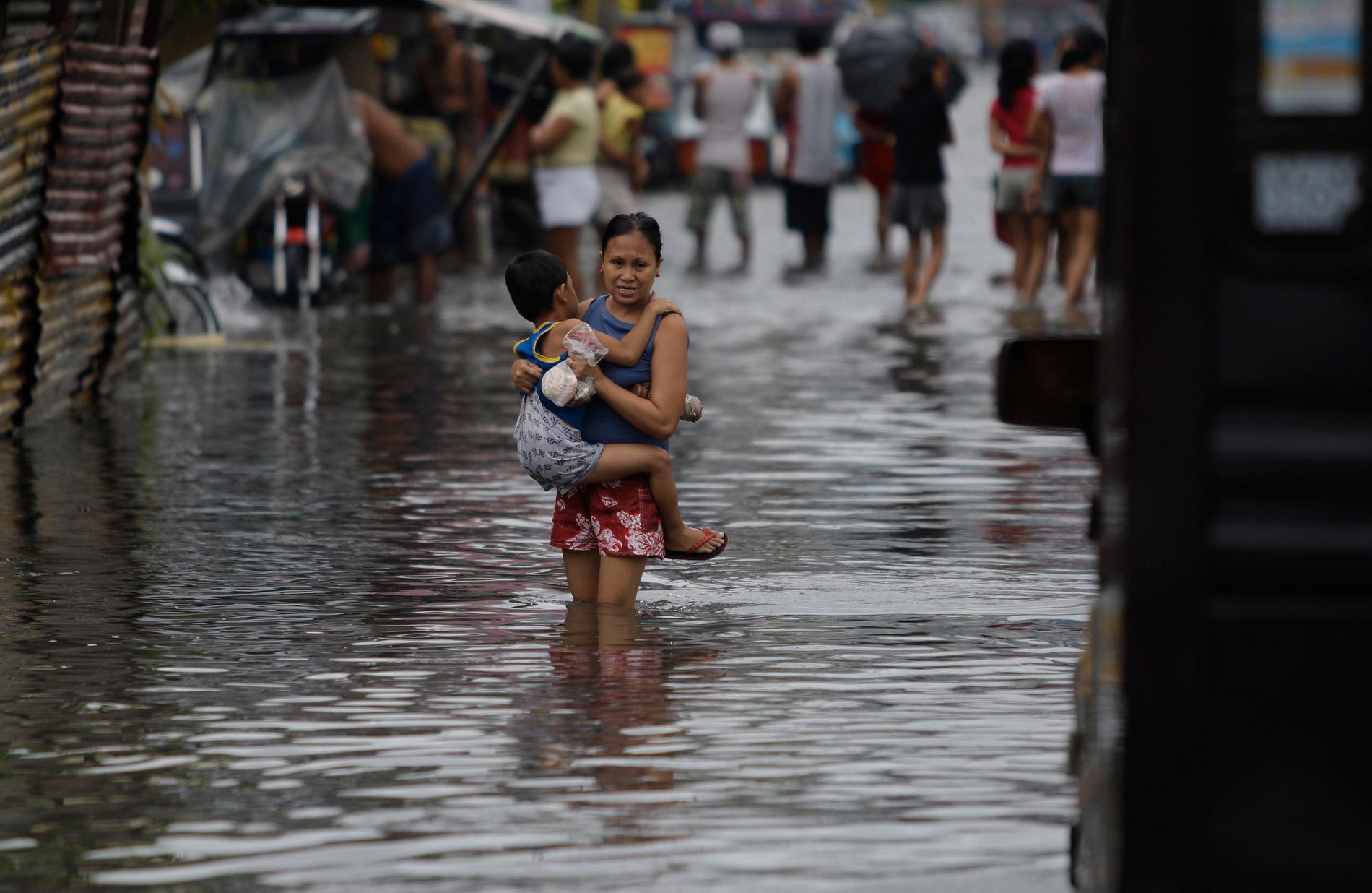 En filippinsk pojke håller fast i sin mamma som korsar en översvämmad gata efter tyfonen Muifas framfart i Manila i Filippinerna. Muifa blåste sedan vidare bort från norra Filippinerna och in över Kina. 