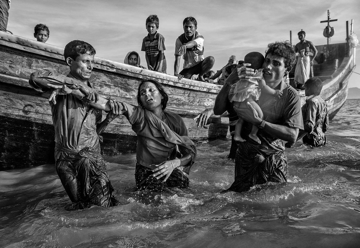 En utmattad kvinna får hjälp av en båt vid Shah porir Dwip efter att ha flytt Burma över floden Naf.