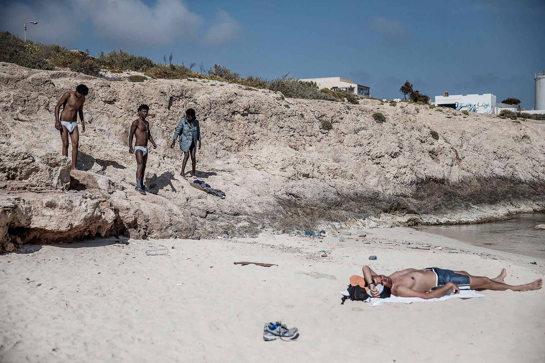 Lampedusa, ön som ligger mitt i medelhavet och blivit en av de första anhalterna för båtflyktingar.  Robel, Nohom, Meron, Anbesa, Amanuel från Eritrea badar i det kristallblåa vattnet på en av lampedusas stränder. Under dagarna har de möjlighet att lämna det inhägnade lägret de bor i.
