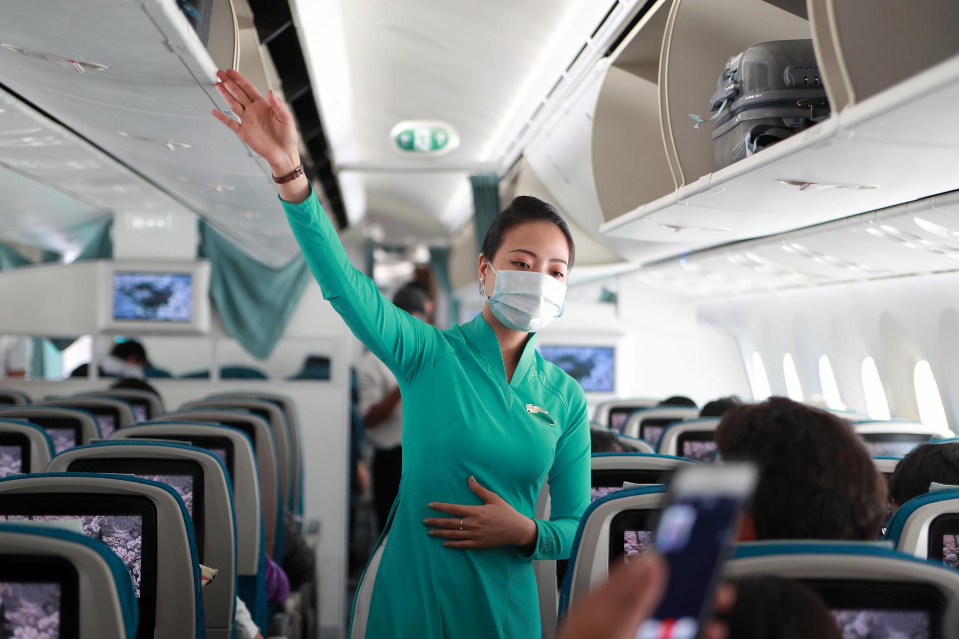 Flygvärdinna med skyddsmask instruerar passagerare på flygplan i Ho Chi Minh-staden i Vietnam. Arkivbild.