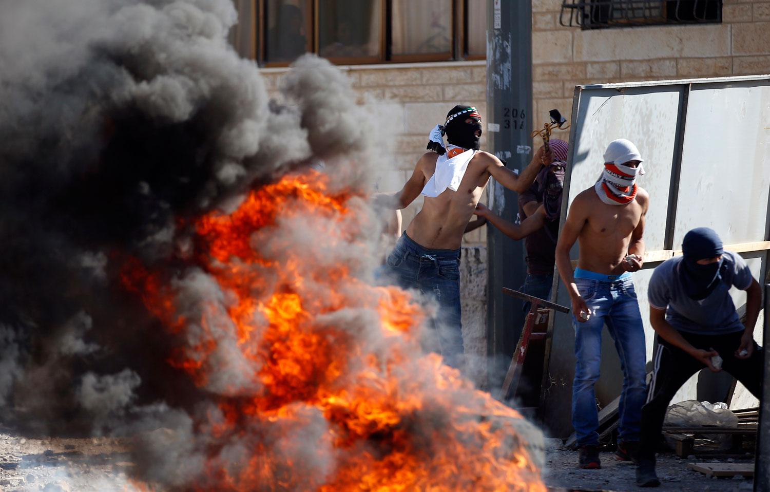 Maskerade palenstinska demonstranter kastar sten mot israelisk polis.