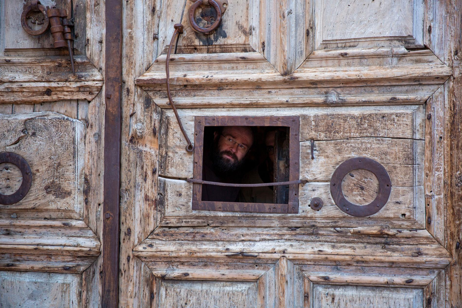 En präst kikar ut genom ett litet fönster i porten till Heliga gravens kyrka i Jerusalem.