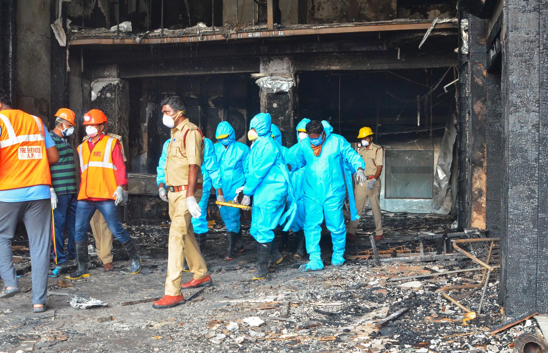 Räddningsarbetare i skyddskläder bär ut en kropp från det elddrabbade hotellet Swarna Palace.
